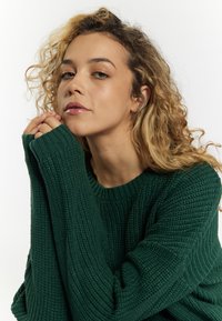 Maglione verde a maglia con motivo testurizzato, polsini a coste e scollatura rotonda. Le maniche lunghe superano i polsi per un fit morbido.