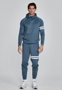 Blue athletic hoodie with drawstring hood and front pocket; matching joggers featuring white stripes and logo on the leg; smooth texture.