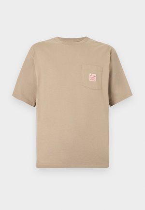 Beige T-shirt med korte ærmer, rund hals og brystlomme med en lille hvid og rød rektangulær lap.