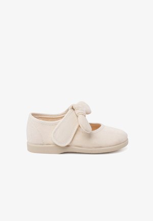 Chaussure en textile beige avec un bout arrondi, un détail de nœud en sangle élastique et une semelle plate douce. La tige présente une finition lisse et texturée.