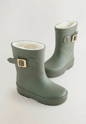 Grüne Gummistiefel mit einem weichen weißen Fellfutter, ausgestattet mit einem goldenen Schnallendetail und einer strukturierten schwarzen Sohle für einen sicheren Halt. Design in mittlerer Schafthöhe.