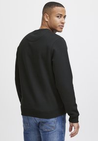Sudadera negra con cuello redondo, puños y dobladillo de canalé, combinada con unos jeans de mezclilla azul. Textura suave y corte casual.