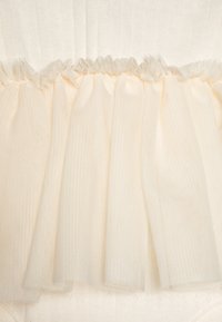 Tissu ivoire transparent avec des volants froncés en haut ; texture en maille légère ; peut être utilisé pour des rideaux ou des accents décoratifs.