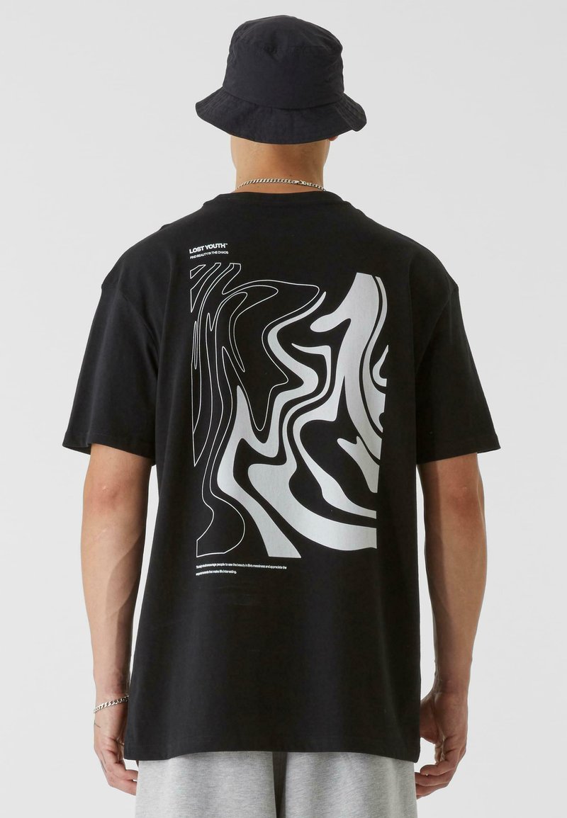 Black cotton t-shirt featuring a wavy white graphic design on the back. Completed with short sleeves and a relaxed fit. Black bucket hat included.