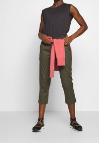 Top sin mangas gris oscuro, pantalones cortos color oliva y sudadera rosa atada a la cintura, combinados con sandalias negras de tiras.