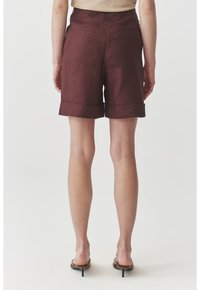 Burgundy linen shorts with a relaxed fit, featuring a cuffed hem and two back pockets. Smooth texture with a subtle sheen.