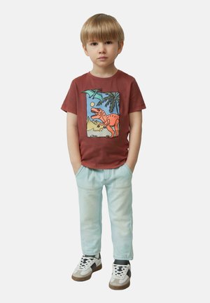 Rotes Baumwoll-T-Shirt mit Dinosaurier-Graphic, kombiniert mit hellblauen Jeans und Turnschuhen. Das Shirt hat einen runden Halsausschnitt und kurze Ärmel.