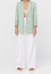 Blazer double boutonnage vert menthe à manches trois-quarts, en tissu texturé, associé à un pantalon large blanc et des sandales à plateforme marron.