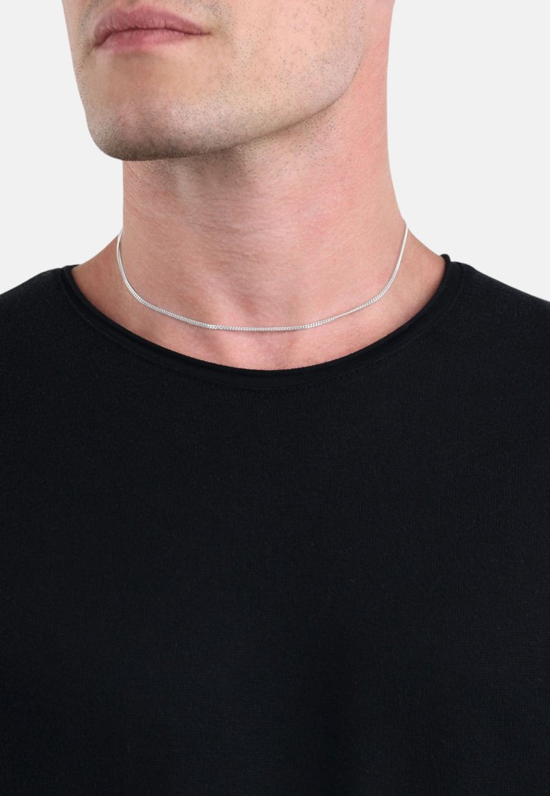 Collana choker in metallo argentato con un design sottile e liscio, indossata al collo, abbinata a una maglietta nera a girocollo.