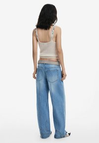 Top en maille cropped beige clair avec des bretelles florales, associé à un jean en denim bleu clair ample, doté de grandes poches et de détails de plis subtils.