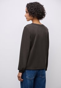 Dunkelgraues Langarmoberteil mit Rundhalsausschnitt, glatter Textur und Raffung an den Ärmelbündchen, kombiniert mit hellblauen Denim-Hosen.