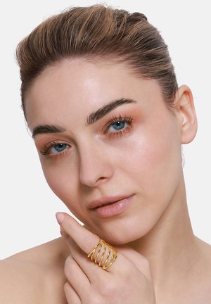 Goldener Metalring mit fünf spiralförmigen Bändern, der an einem Finger getragen wird, zeigt eine glatte, glänzende Oberfläche vor einem neutralen Hintergrund.
