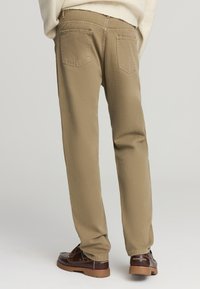Pantaloni di cotone beige a gamba dritta, con tasche posteriori e finitura pulita. Indossati con scarpe di pelle marroni.