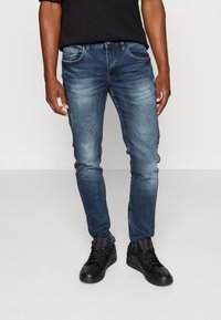 Vaqueros de mezclilla azul con un corte ajustado, que presentan un desgaste sutil y cinco bolsillos, combinados con zapatillas altas negras.