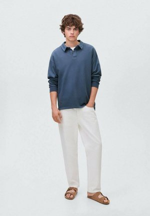 Marineblauwe lange mouwen polo, witte losse broek en bruine sandalen. Heeft een ontspannen pasvorm en een zachte stoftextuur.