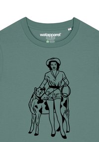 Grünes Baumwoll-T-Shirt mit schwarzem Grafikdruck einer Frau in Shorts, die ein Kuhhalfter hält. Einfaches Design mit Rundhalsausschnitt und kurzen Ärmeln.
