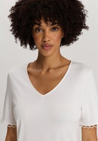 Top bianco a maniche corte con scollatura a V e orlo scallopato sulle maniche, realizzato in un tessuto morbido e liscio, che presenta una vestibilità comoda.