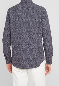 Námořnická modrá košile s dlouhým rukávem, drobným květinovým vzorem, zapínáním na manžety, zakřiveným lemem a hladkou texturou látky.