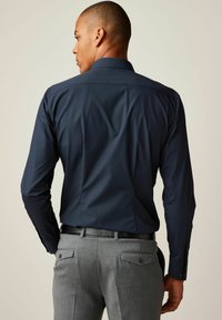 Marineblauw shirt met lange mouwen, een aansluitend ontwerp, met knoopmanchetten en een soepele stof, gecombineerd met grijze op maat gemaakte broeken met achterzakken.