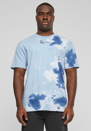 Svetlo modré tričko s tye-dye vzorom, s modrými škvrnami, krátkymi rukávmi a okrúhlym výstrihom. Obsahuje malé čierne podpisové logo na hrudi.