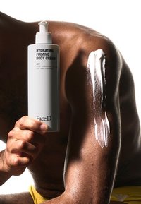 Bottiglia bianca di Crema Idratante e Rassodante per il Corpo con testo grigio tenuta in mano, lozione cremosa applicata su pelle marrone. Texture liscia, forma cilindrica.