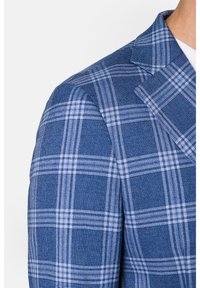 Niebieska marynarka w kratę z teksturowanej tkaniny, z białymi wzorami w kratkę i dopasowanym kołnierzem, podkreślająca wyraźne ramiona.