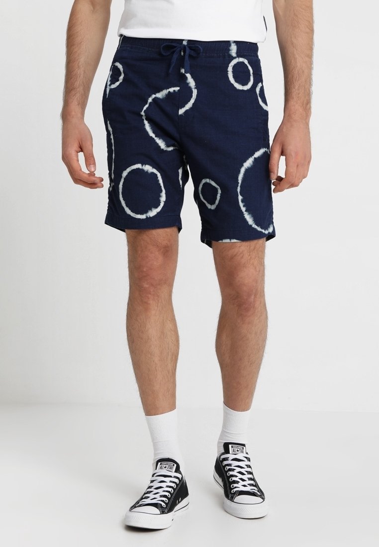 Námorně modré šortky s bílými vzory kroužků ve stylu tie-dye. Vyrobené z prodyšné tkaniny, s elastickým pasem a stahovací šňůrkou.