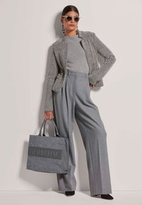 Grau melierter Blazer mit geometrischem Muster, kombiniert mit grauen, taillierten weiten Hosen und einer grauen Tote-Tasche mit einprägtem Schriftzug.