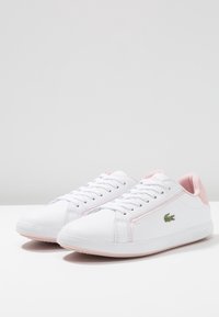 Baskets en cuir blanc avec des accents roses, dotées d'une semelle plate, d'un bout arrondi et d'un emblème de logo sur le côté. Fermeture à lacets.