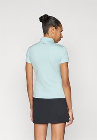 Ljusblå pikétröja med korta ärmar och krage, svart kjol, slät textur, logodetalj på baksidan nära halsringen.