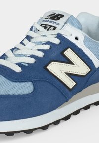 Синьо-бял маратонка New Balance 574 с бели връзки, мрежести и велурени детайли и гумена подметка.