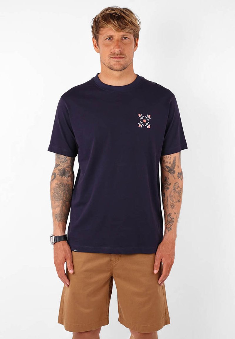 T-shirt en coton bleu marine à manches courtes et col rond, présentant un petit motif géométrique multicolore sur la poitrine gauche.