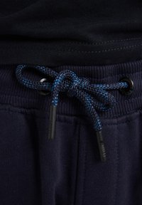 Marineblaue Sweatpants verfügen über einen strukturierten Bund mit einem Kordelzug aus geflochtenem blauen und schwarzen Material, gesichert mit Plastikkappen.