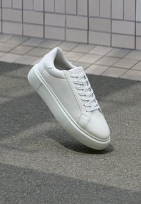 Weiße Ledersneaker mit flachem Schnürverschluss, runder Spitze und strukturiertem Gummisohle. Einfaches, minimalistisches Design ohne sichtbare Logos.