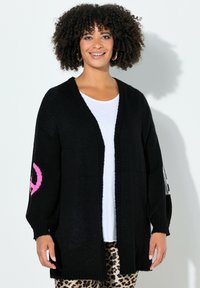 Sort cardigan med løs pasform, prydet med et pink fredssymbol på et ærme. Strikket tekstureret stof med V-halsdesign. Kombineret med leopardprint bukser.