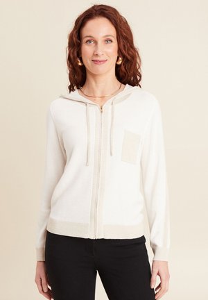 Cream hoodie cardigan with a zip front, textured knit, ribbed cuffs, and a small patch pocket in a lighter shade of cream.
