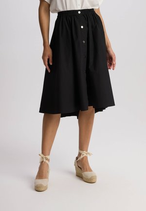 Czarna spódnica do kolan z marszczonym pasem, z przodu na guziki, wykonana z miękkiej bawełny. Noszona z beżowymi espadrylami na koturnie.
