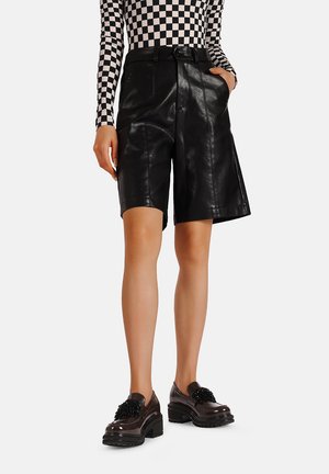 Pantaloni di pelle nera con vita alta, passanti per la cintura e tasche laterali. Abbinati a una camicia a maniche lunghe a quadri e scarpe nere con suola spessa.