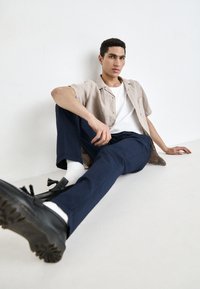 Casual outfit featuring a beige linen short-sleeve shirt, white T-shirt, navy trousers, and black shoes with tassel accents.