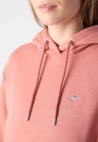 Felpa rosa in cotone con una superficie texture. Presenta un cappuccio con cordino, dettagli in metallo argentato e un piccolo logo ricamato.