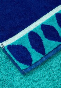 Serviette turquoise et bleu marine avec une surface texturée, présentant un motif de vagues sur un bord et une section solide en tissu éponge en peluche.