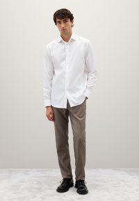 Camicia bianca a maniche lunghe con bottoni, in tessuto leggero e strutturato, abbinata a pantaloni grigi. Scarponi neri con lacci. Design semplice e colori neutri.