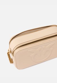 Pochette in pelle beige con doppia cerniera, logo impresso e hardware dorato. Texture liscia con dettagli in cucitura bianca.