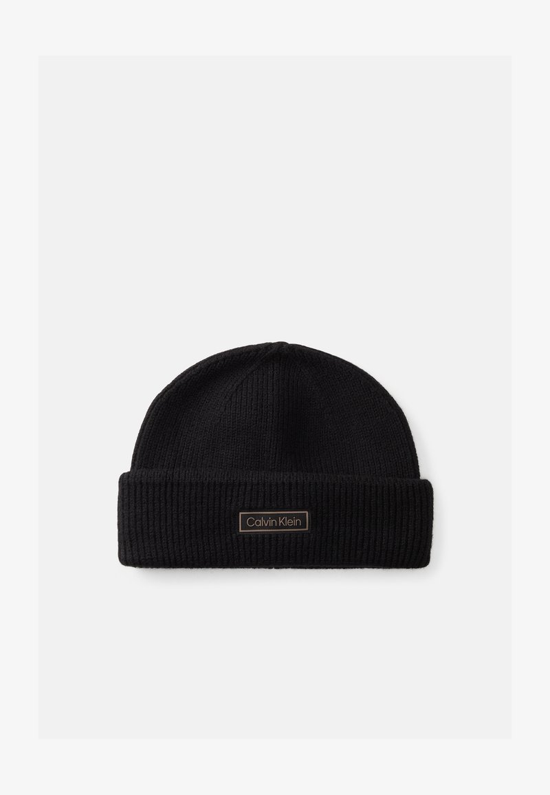 Must mustrüüga must kootud beanie, millel on volditud serv ja ees pronksist ristküliku kujuline logo silt.