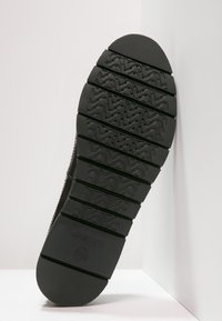 Semelle de chaussure en caoutchouc noir avec des motifs de bande de roulement profonds, comprenant des rainures et des crêtes pour l'adhérence, et un bord plat sur les côtés.