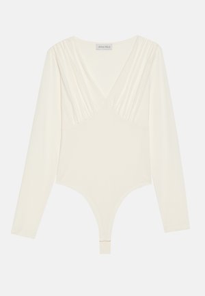Bodysuit à manches longues en crème, avec un décolleté en V profond, une texture froncée aux épaules et un design de culotte tanga. Tissu doux et extensible.