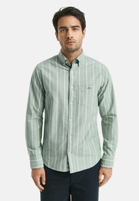 Camicia button-up di colore verde chiaro con righe verticali bianche. Presenta colletto, maniche lunghe e una tasca sul petto con un piccolo dettaglio del logo.