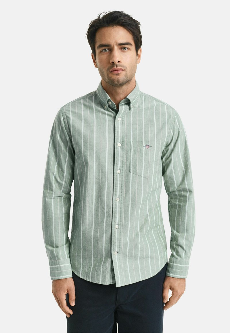 Camicia button-up di colore verde chiaro con righe verticali bianche. Presenta colletto, maniche lunghe e una tasca sul petto con un piccolo dettaglio del logo.