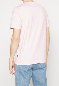 Short-sleeve t-shirt in light pink cotton, crew neck, featuring a small label on the hem, paired with light blue denim jeans.