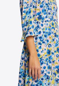 Kwiecista sukienka z żywym niebiesko-żółtym wzorem na lekkim materiale, o zwiewnym kroju i rozszerzanych rękawach.